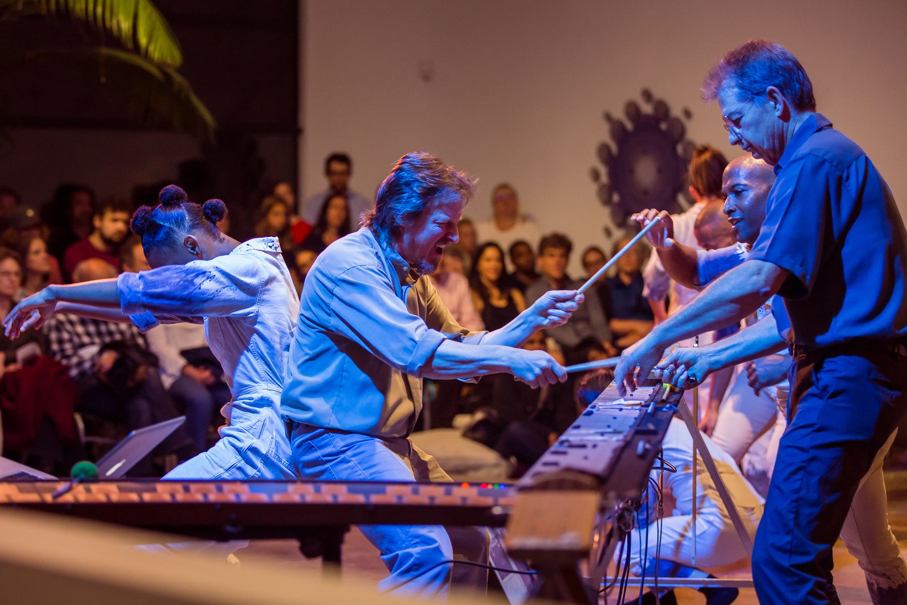 Joel Davel playing the Marimba Lumina in performance, with dancers and audience close around him